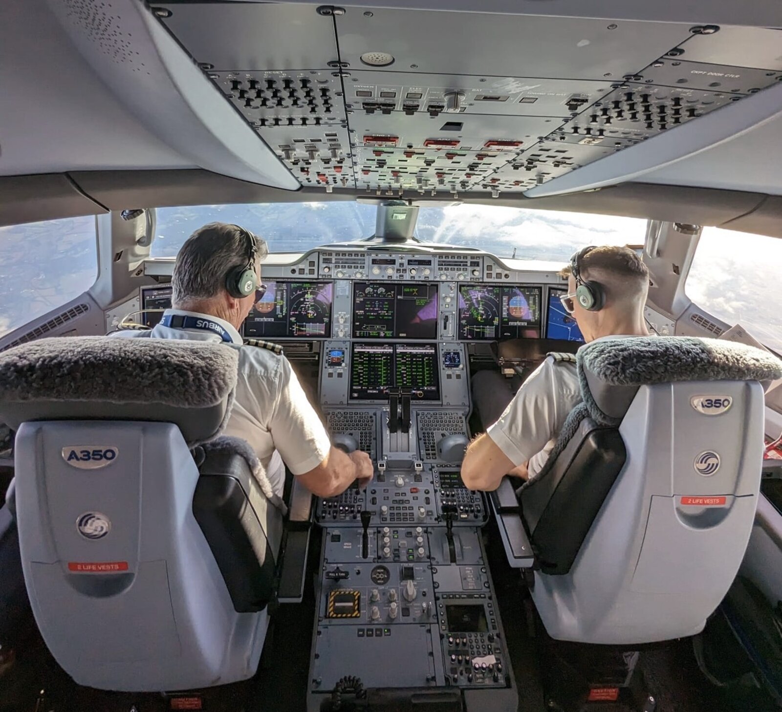 Two pilots at the controls on an Airbus A350 flight deck, seen from behind