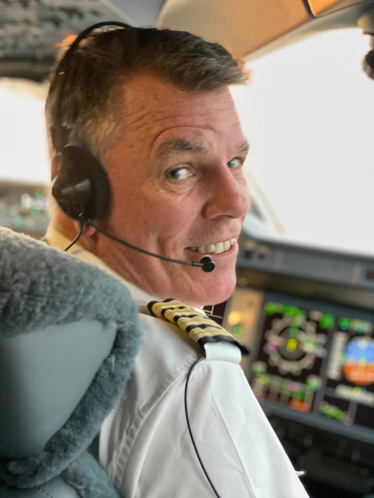 Captain Chris Pohl smiling over his shoulder in the cockpit, wearing his captain's uniform and headset